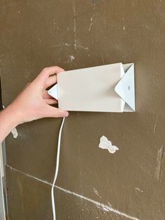 a hand is holding an open box with wires coming out of it and plugged into the wall