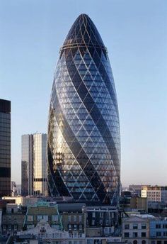 a very tall glass building in the middle of a city with other buildings around it