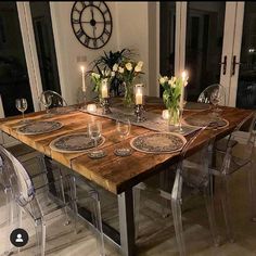 a wooden table topped with lots of plates and glasses next to candles on top of glass chairs