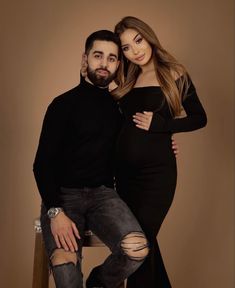 a man and woman pose for a photo in front of a brown background with their arms around each other