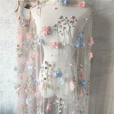 a white dress with flowers on it is hanging from a rack in front of a wall