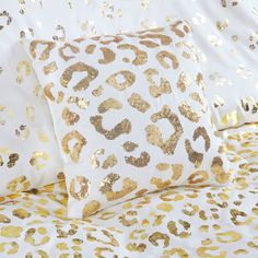 two white and gold pillows on top of a bed covered in animal print sheets with golden sequins