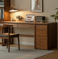 a wooden desk topped with a laptop computer next to a lamp and bookshelf