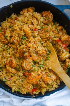 a skillet filled with shrimp and rice on top of a white cloth next to a wooden spoon