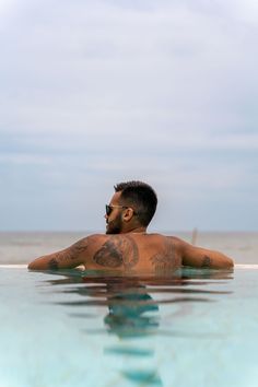 a man sitting in the water with his back turned to the camera and tattoos on his chest