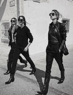 three young women walking down the street in black leather jackets and sunglasses, with one woman wearing