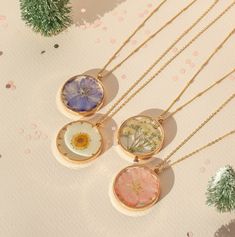 three necklaces with flowers on them sitting next to some pine cones and confetti