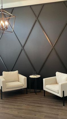 two white chairs sitting next to each other in front of a wall with geometric designs