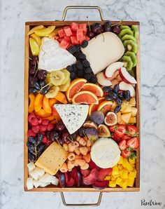 an assortment of fruits and cheese in a wooden tray on a marble counter top with a metal frame