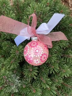 a pink ornament hanging from the top of a pine tree with ribbon on it