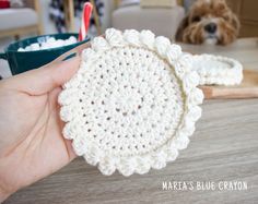 a crocheted dishcloth being held by a person with a dog in the background