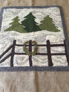 a knitted placemat with a fence and trees on the front, along with a wreath