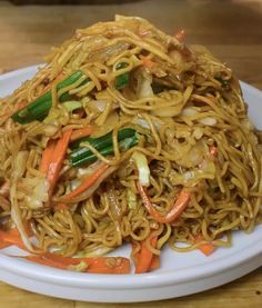 a white plate topped with noodles and veggies on top of a wooden table