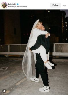 a man holding a woman in his arms while she is walking down the street at night