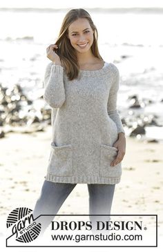 a beautiful young woman standing on top of a sandy beach next to the ocean wearing a sweater