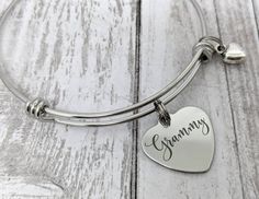 "This is an stainless steel bangle bracelet with an 18mm stainless steel heart charm that reads, \"Grammy.\" All items will arrive boxed and ready for gift giving." Personalized Stainless Steel Heart Bracelet For Mother's Day, Personalized Stainless Steel Heart Bracelet As Gift, Gift Bracelet With Heart Charm In Stainless Steel, Gift Stainless Steel Bracelets With Heart Charm, Stainless Steel Bracelets With Heart Charm As Gift, Personalized Adjustable Stainless Steel Heart Bracelet, Adjustable Stainless Steel Heart Bracelet For Anniversary, Custom Name Heart Bracelet For Mother's Day Gift, Mother's Day Gift Stainless Steel Name Bracelet