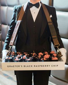 a man in a tuxedo is holding a tray with cupcakes on it