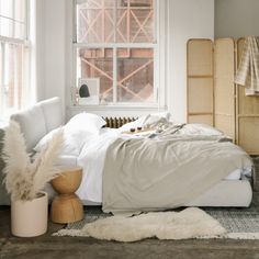 a white bed sitting next to a window in a room with lots of pillows and blankets