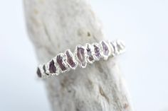 a silver ring with amethorate stones on it's side sitting on top of a piece of driftwood