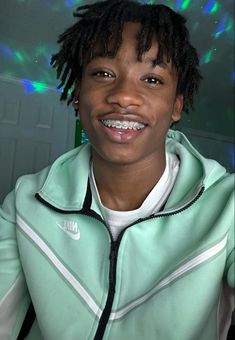 a young man with dreadlocks smiles at the camera while wearing a nike jacket