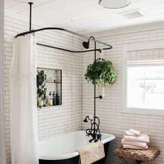 a bathroom with white brick walls, black tub and plants on the shower curtain rod