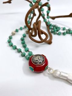 "This Tibetan pendant has a silver Ganesh on a red coral pendant with inlaid turquoise details. The chain is turquoise rosary bead chain and joined with white vintage mosaic Tibetan beads, finished with a white silk tassel. - The necklace is 32\" long - The charm is 1.25\" in diameter - White silk Tassel is 4\" long * * * * * * * Connect with WTB on social media! Instagram: @whatthebuckle Facebook: What the Buckle Twitter: @Whatthebuckle" Bohemian Turquoise Necklace With 108 Beads For Gift, Spiritual Turquoise Necklace With Silver Beads, Bohemian Silver Turquoise Necklace With Beaded Chain, Silver Bohemian Turquoise Necklace With Beaded Chain, Silver Jewelry With 108 Beads For Festivals, Artisan Turquoise Necklace With Silver Beads As Gift, Traditional Turquoise Necklaces With Beaded Chain, Red Bohemian Jewelry With Silver Beads, Bohemian Red Jewelry With Silver Beads