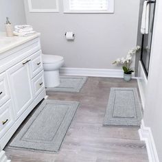 a bathroom with white cabinets and gray rugs