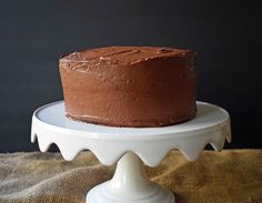 a chocolate cake sitting on top of a white cake platter next to a black wall