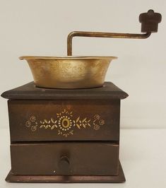 an old fashioned metal grinder on top of a wooden box with a brass bowl