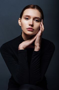 a woman with her hand on her chin, posing for a studio photo in front of a dark background