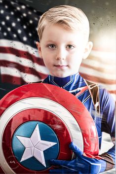 a young boy dressed as captain america holding a shield and an american flag in the background