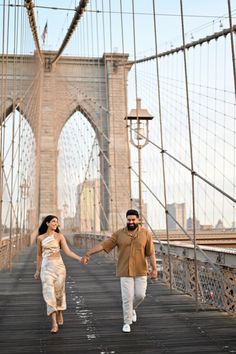 a man and woman walking across a bridge with the brooklyn bridge in the back ground