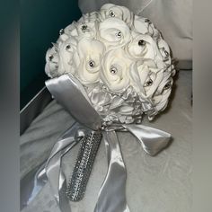 a bridal bouquet with white roses and silver ribbons on a bed sheet, next to a pillow