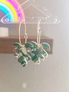 a pair of earrings with green leaves hanging from hooks in front of a rainbow colored background