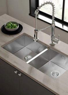 a stainless steel kitchen sink with two faucets and a bowl of green apples