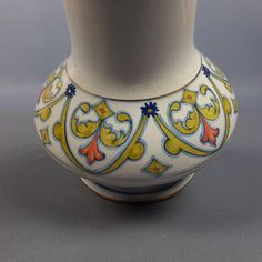 a white vase with yellow and blue designs on the outside, sitting on a gray surface