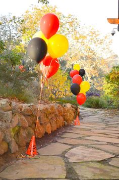 several balloons are floating in the air near a stone wall and walkway with orange cones on it