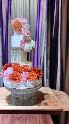 a three tiered wedding cake with flowers on the top and bottom, sitting on a wooden table