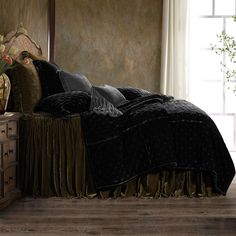 a bed with black and gold comforters in a room next to a window,