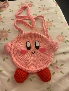 a pink crocheted bag with an adorable face on it's side, sitting on top of a bed