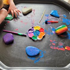 the child is painting with colorful paints on the tray