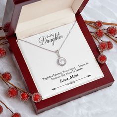 a box with a necklace in it sitting on a table next to some red berries