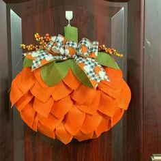 an orange and green pumpkin wreath hanging on a wooden door with gingham checkered bow