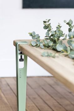 a plant is growing on top of a wooden table with a green metal leg that has an electronic device attached to it