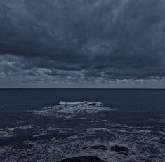 dark clouds over the ocean with waves coming in from the shore and one boat on the water