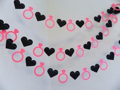 some pink and black paper hearts are hanging on a white wall with the word love spelled out