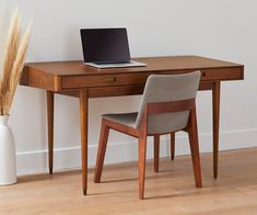 a laptop computer sitting on top of a wooden desk next to a vase filled with dry grass