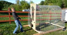 a woman standing next to a large chicken cage in the middle of a grass field