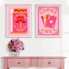 two framed art prints on the wall above a pink table with flowers and vases