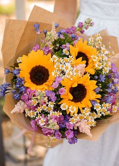 a woman holding a bouquet of sunflowers and purple flowers